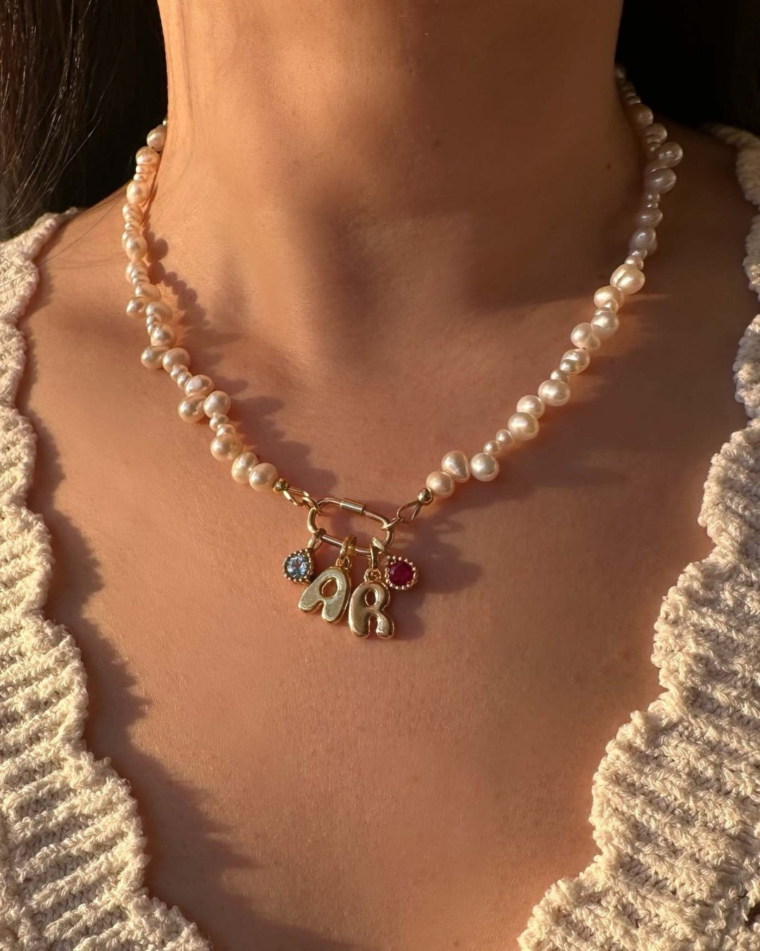 Pearl Carabiner Charm Holder Necklace with bubble initial letters E R and birthstone pendants worn by a woman.