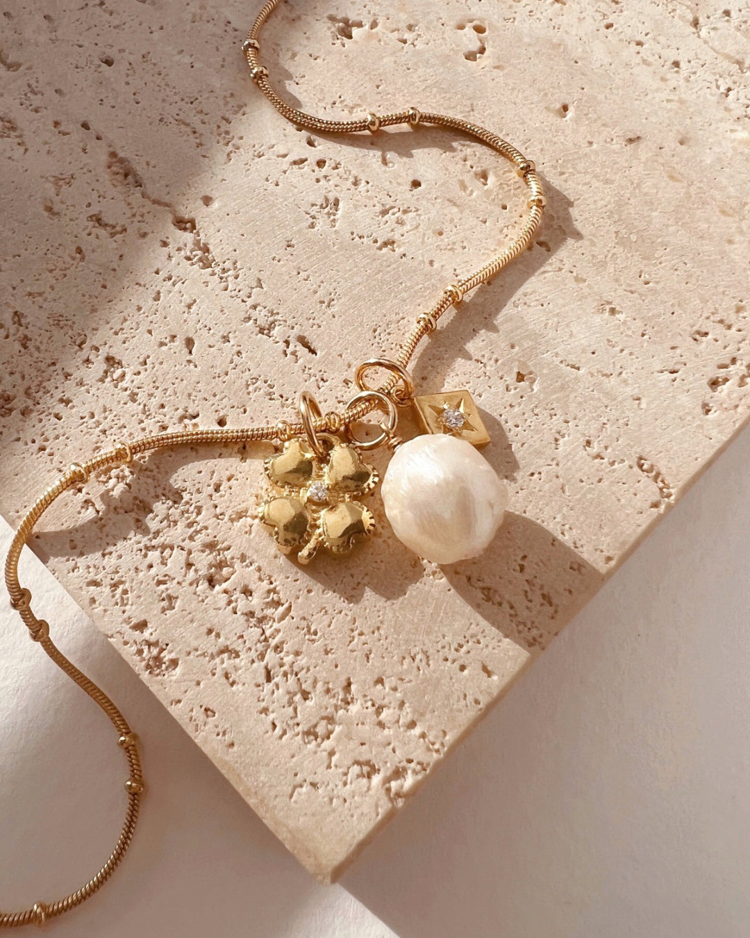 Flatlay of Romyli classic pearl pendant on gold fill bail paired with gold beaded chain, clover talisman pendant and Asteria crystal pendant – layered Australian jewellery styling.