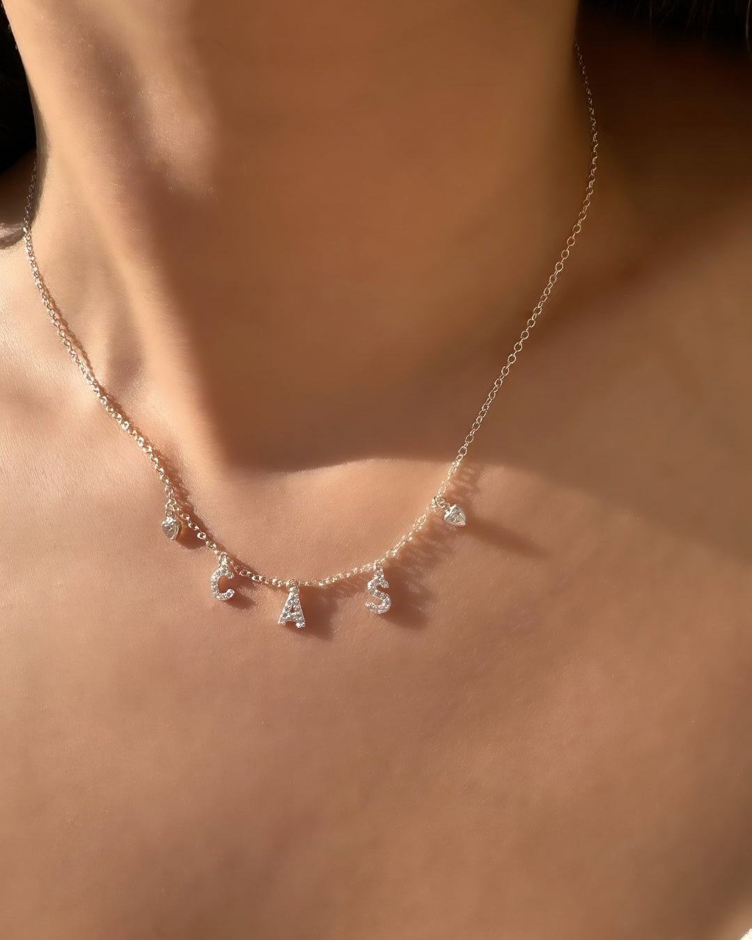 Model wearing silver pavé initial necklace with dainty custom letters and bezel heart charms, personalised sterling silver jewellery for everyday wear