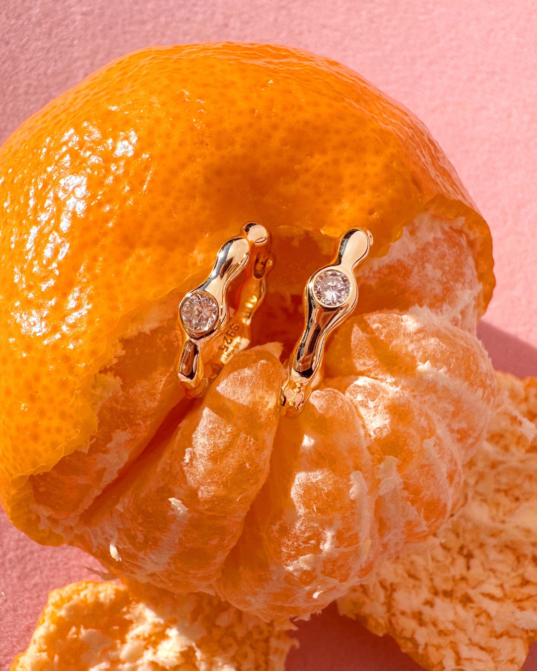 Close-up of Romyli Sculpted Hoops in 18k gold vermeil styled on citrus fruit, showing organic sculpted texture and CZ stone