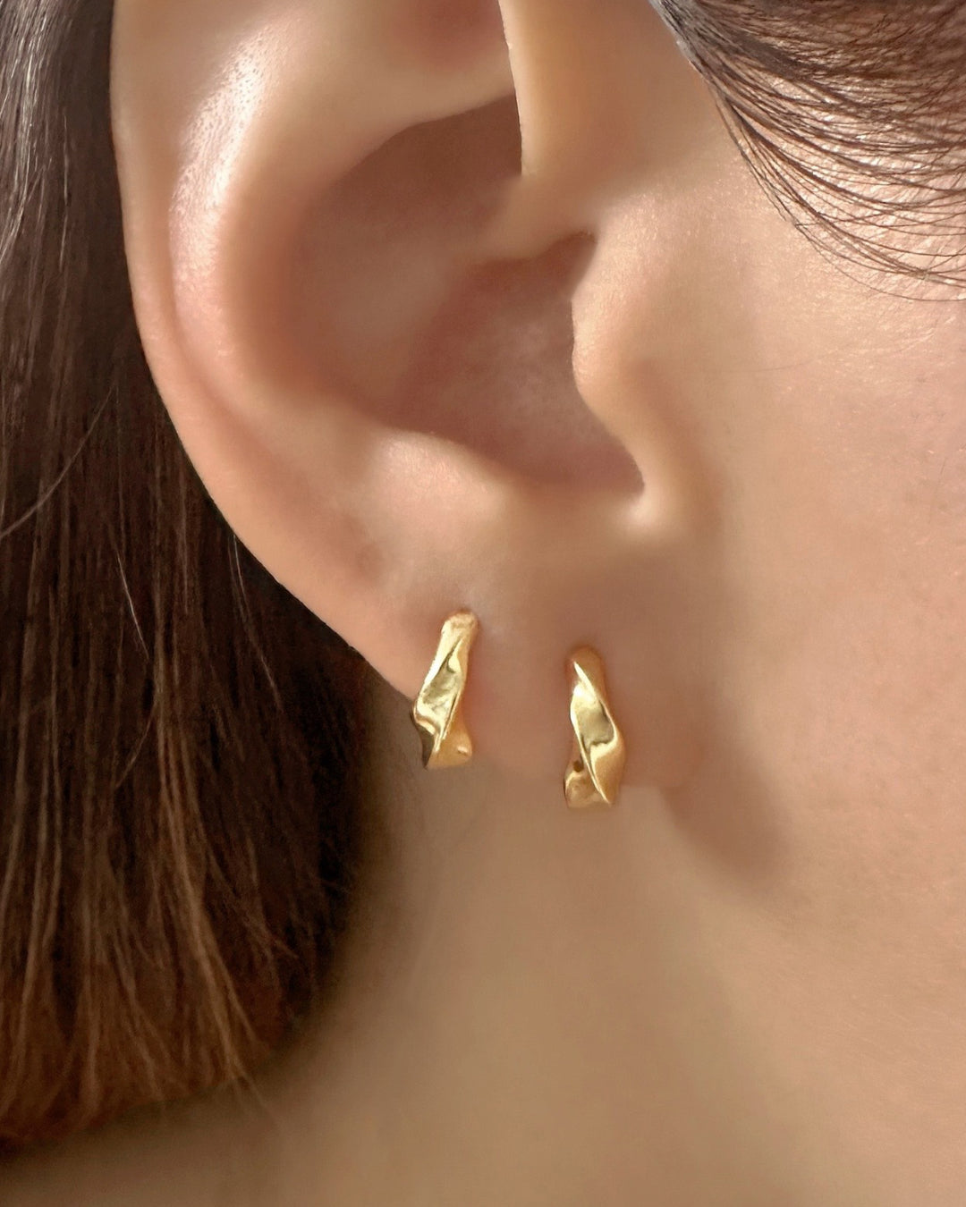 Close-up of a model wearing a pair of gold vermeil Molten Dome Huggie earrings with a blurred background