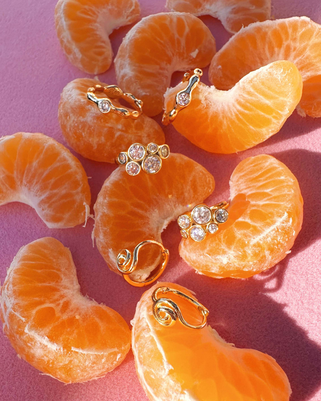 Romyli Sculpted Hoops styled alongside Bubble Cluster Huggies and Spiral Huggies on citrus fruit flat lay