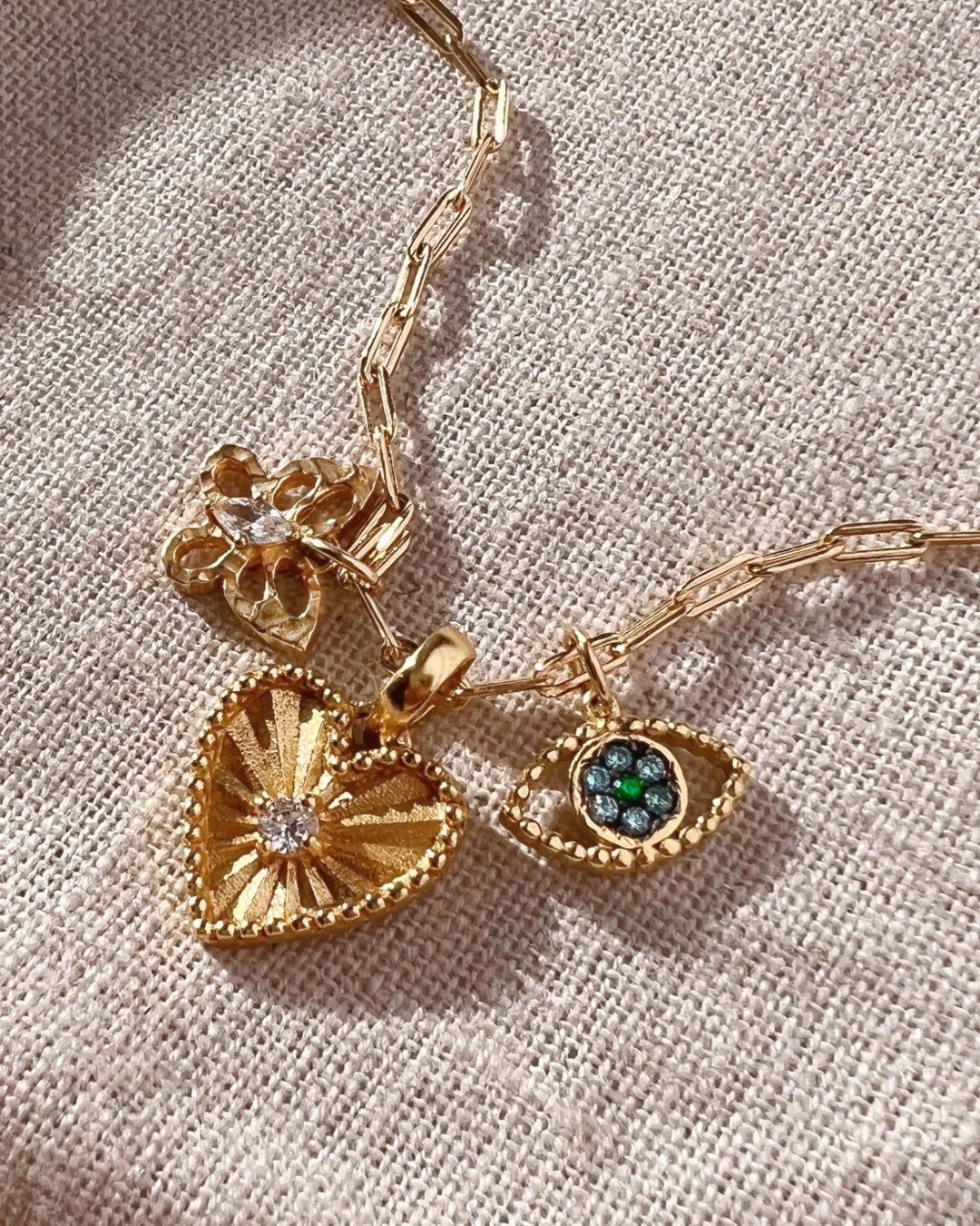 Gold paperclip chain necklace paired with the textured butterfly pendant, heart token pendant and evil eye pendant.