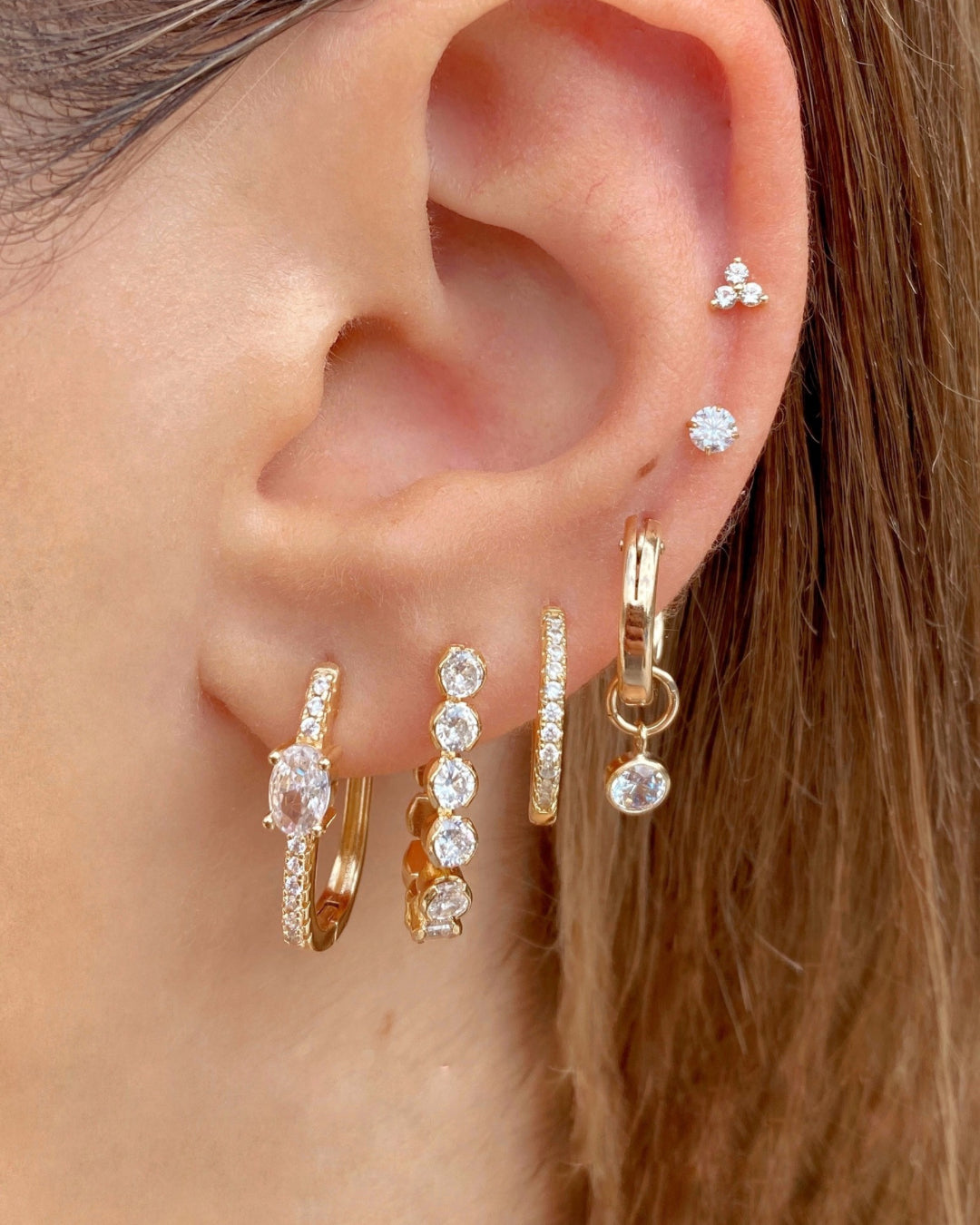 Gold cubic zirconia charm hoops stacked with a range of gold and crystal hoops and earring studs 