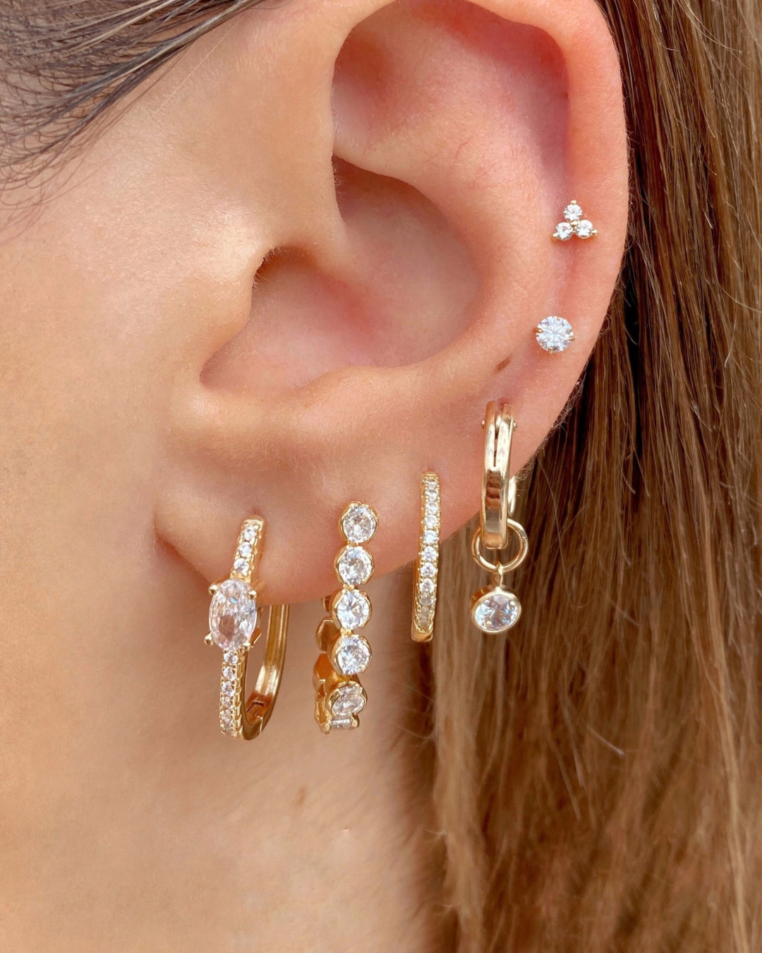Gold cubic zirconia charm hoops stacked with a range of gold and crystal hoops and earring studs
