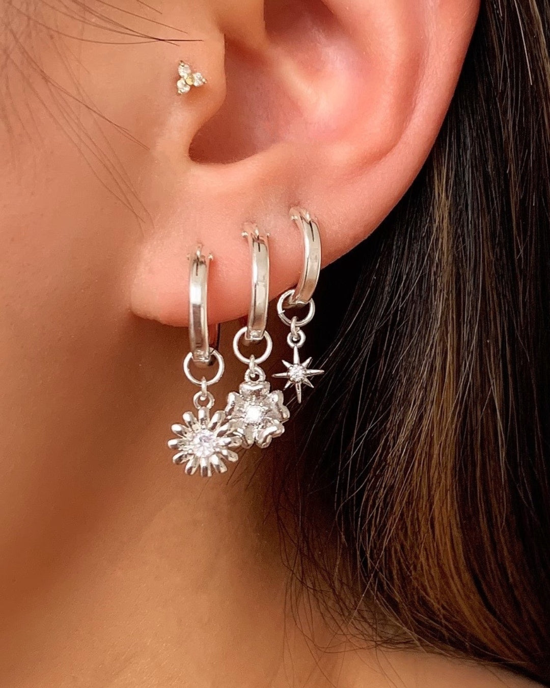 Sterling Silver Small Hoop Earrings with Silver Daisy, Fleur and North Star Earring Charms on a model.