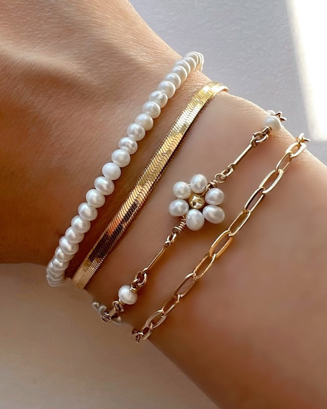 Gold Daisy Pearl Bracelet stacked with gold and pearl bracelets on a model