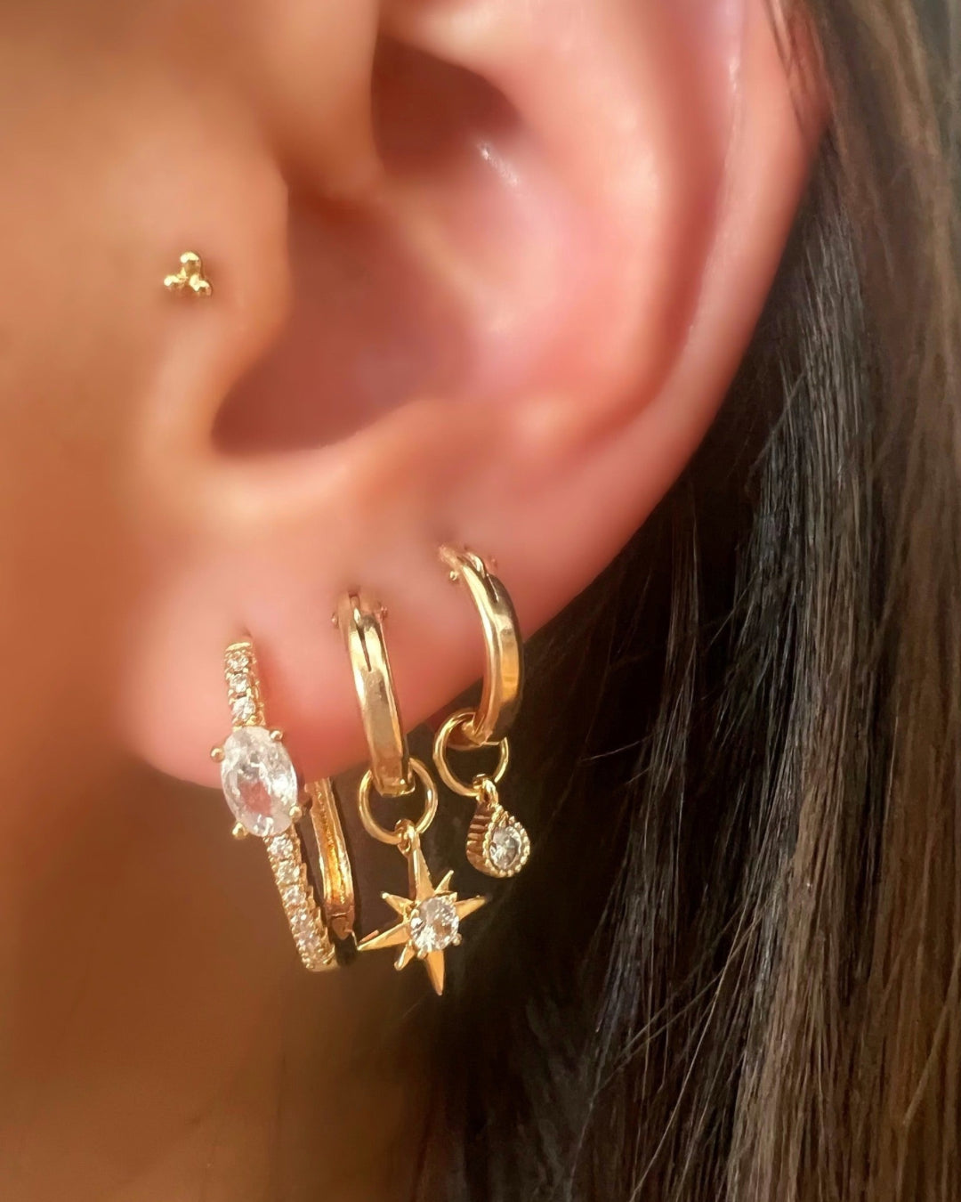 Gold North Star charm hoop earrings on a model