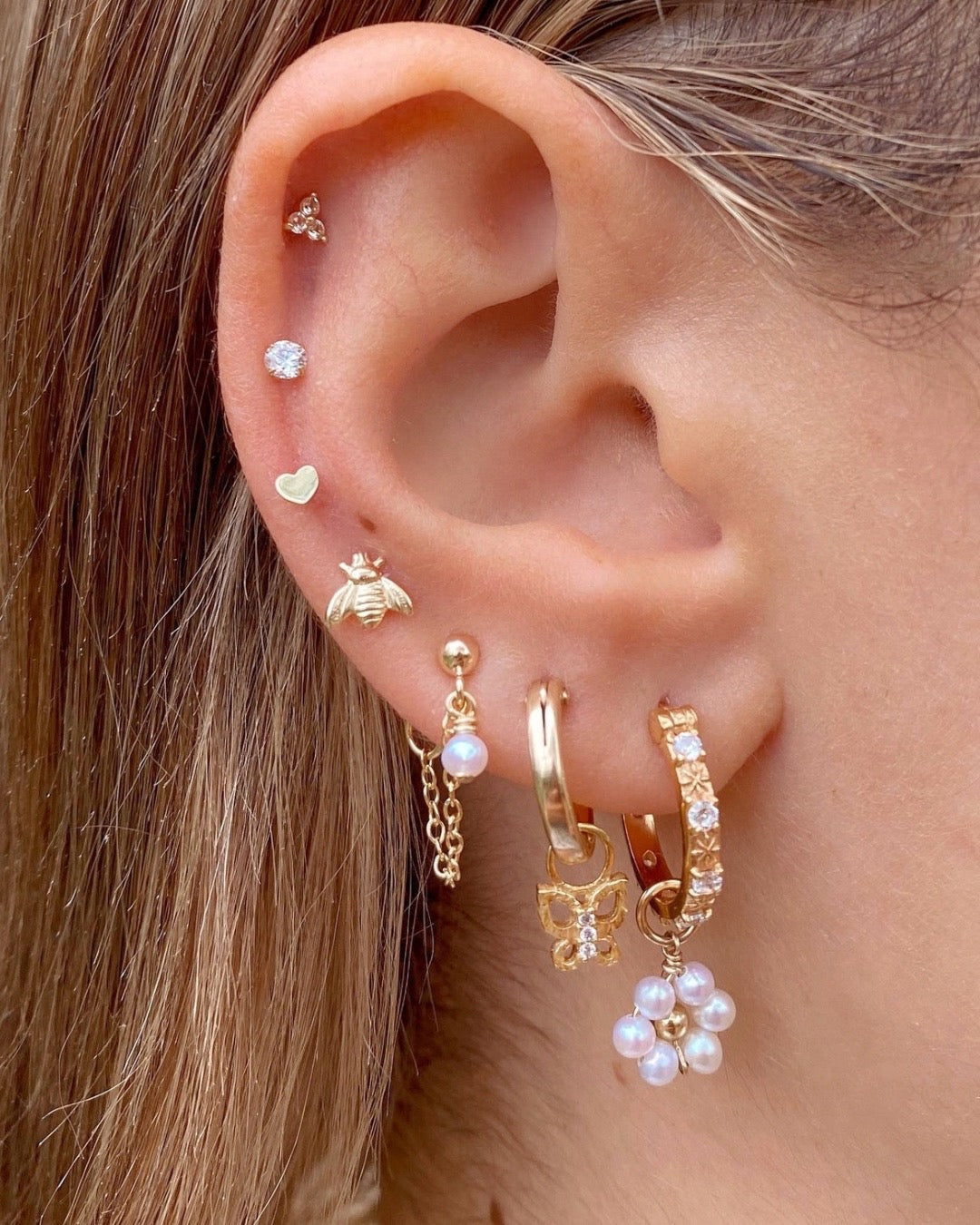Gold hoop earrings with textured butterfly charms adorned with pave crystals, designed with removable charms for versatile styling from minimal to statement looks. Styled on a model.