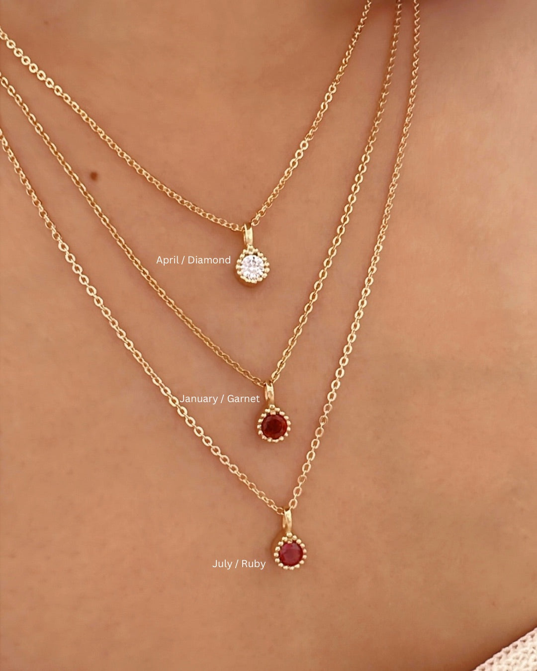 Gold July Birthstone Necklace layered with April White Diamond Birthstone Necklace and January Red Garnet Birthstone Necklace on a model