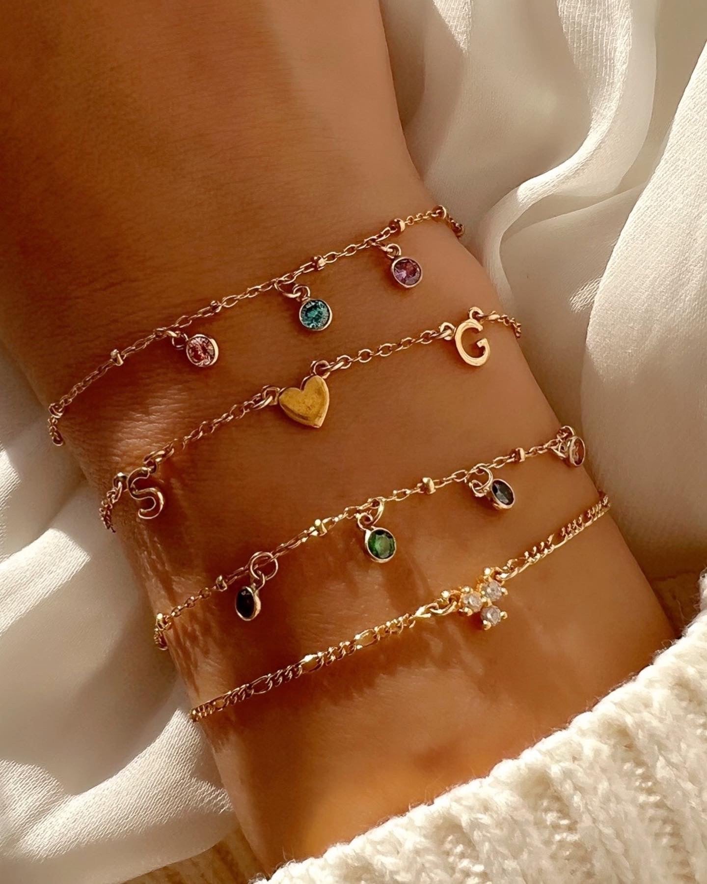 Customizable gold petite initial bracelet with the option to add up to 5 letters, gems or heart