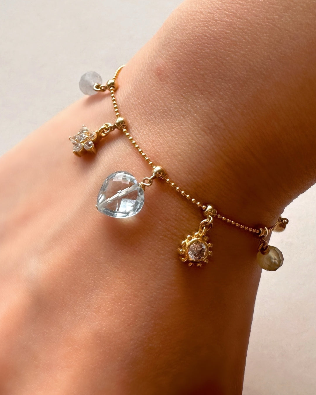 Model wearing 14k Gold Fill Charm Story Bead Chain Bracelet with Sola Sun Charm, Flora Charm and Blue Topaz Charm