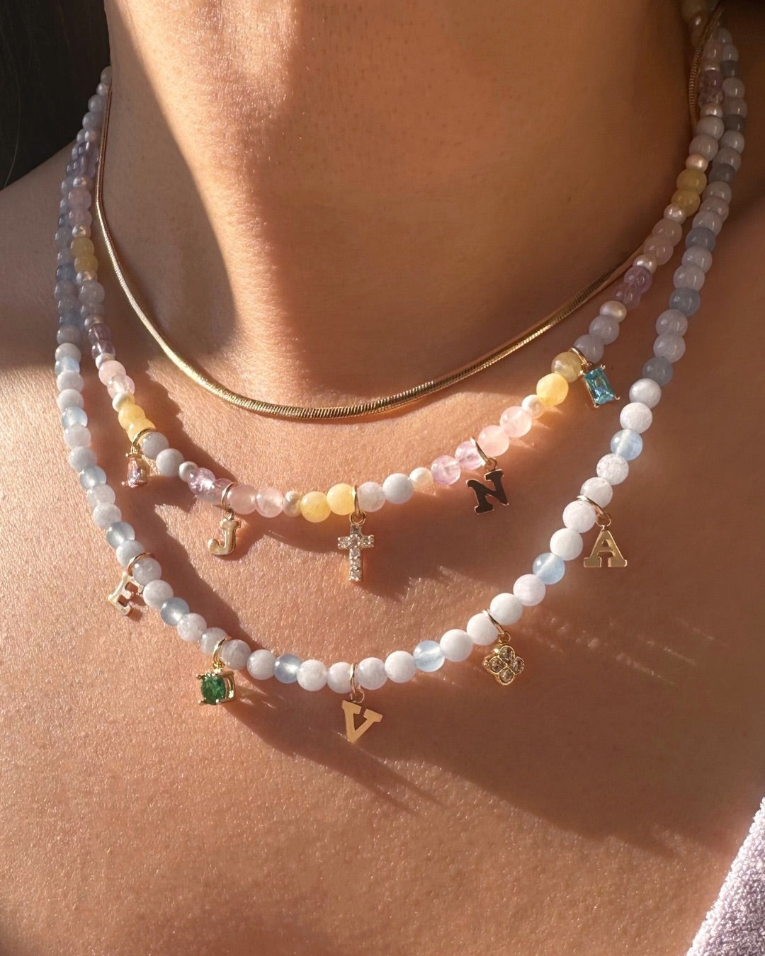 Close-up of a person wearing 2 gemstone necklaces with charms on a light background