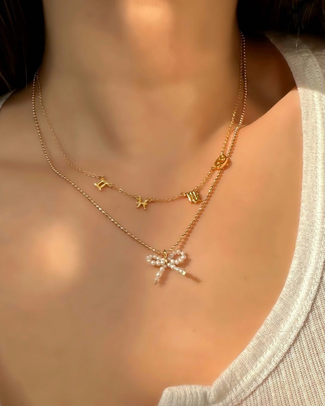 Petite Freshwater Pearl Bow Pendant on a Gold Satellite Chain Necklace layered with a Zodiac Necklace on a model 
