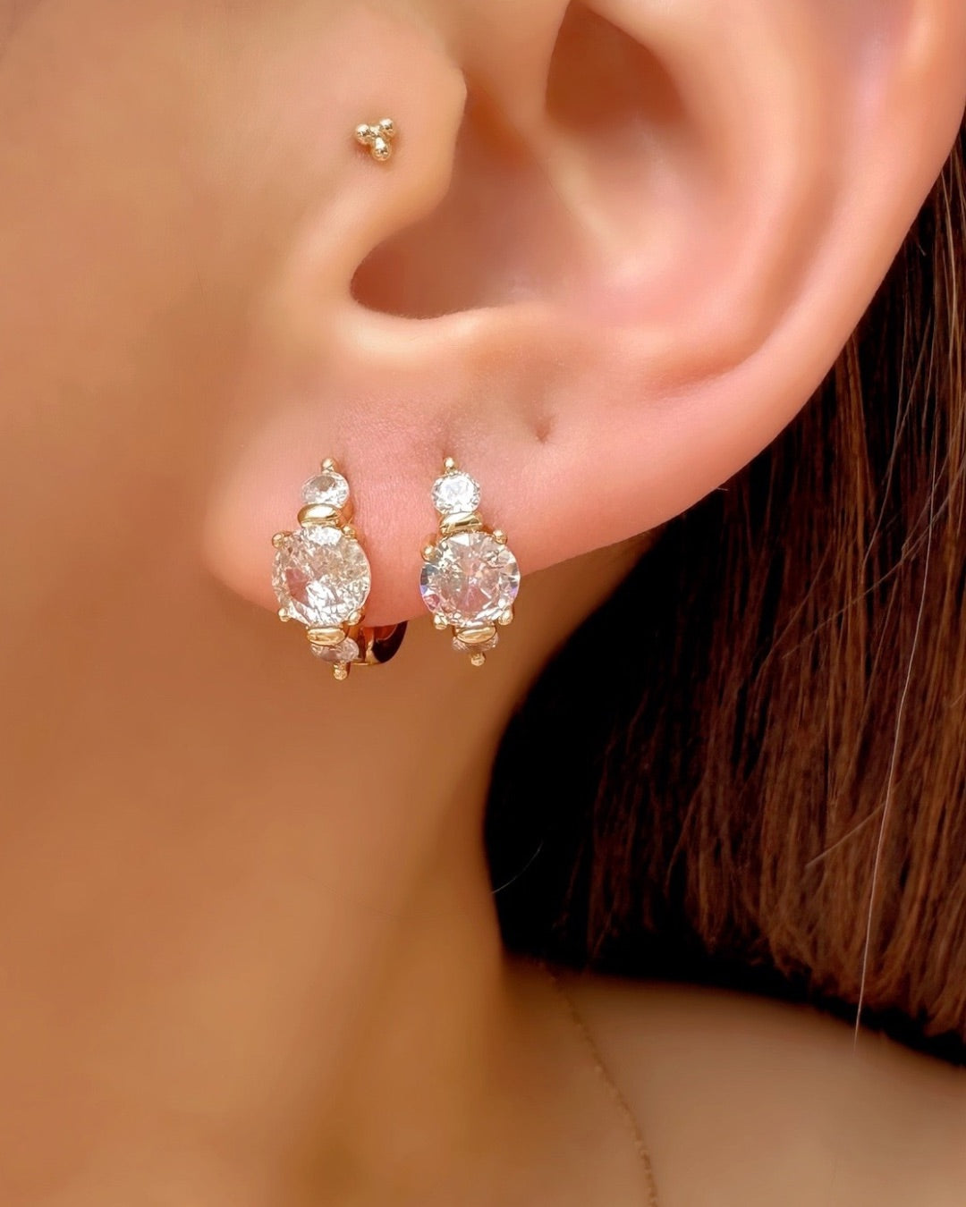 Close-up of an ear wearing a pair of gold Celeste trio hoop earrings with clear gemstones.