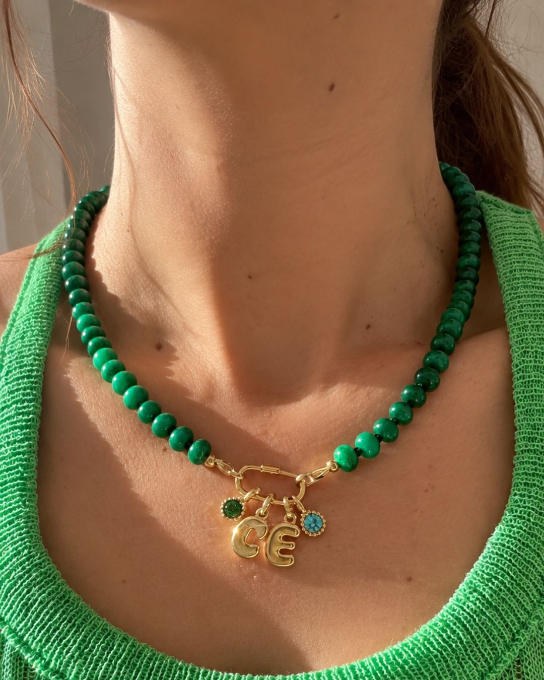 Model wearing an emerald green Jade beaded charm necklace with bubble initial C and E, together with an Emerald May Birthstone and Blue Topaz December birthstone pendant. 