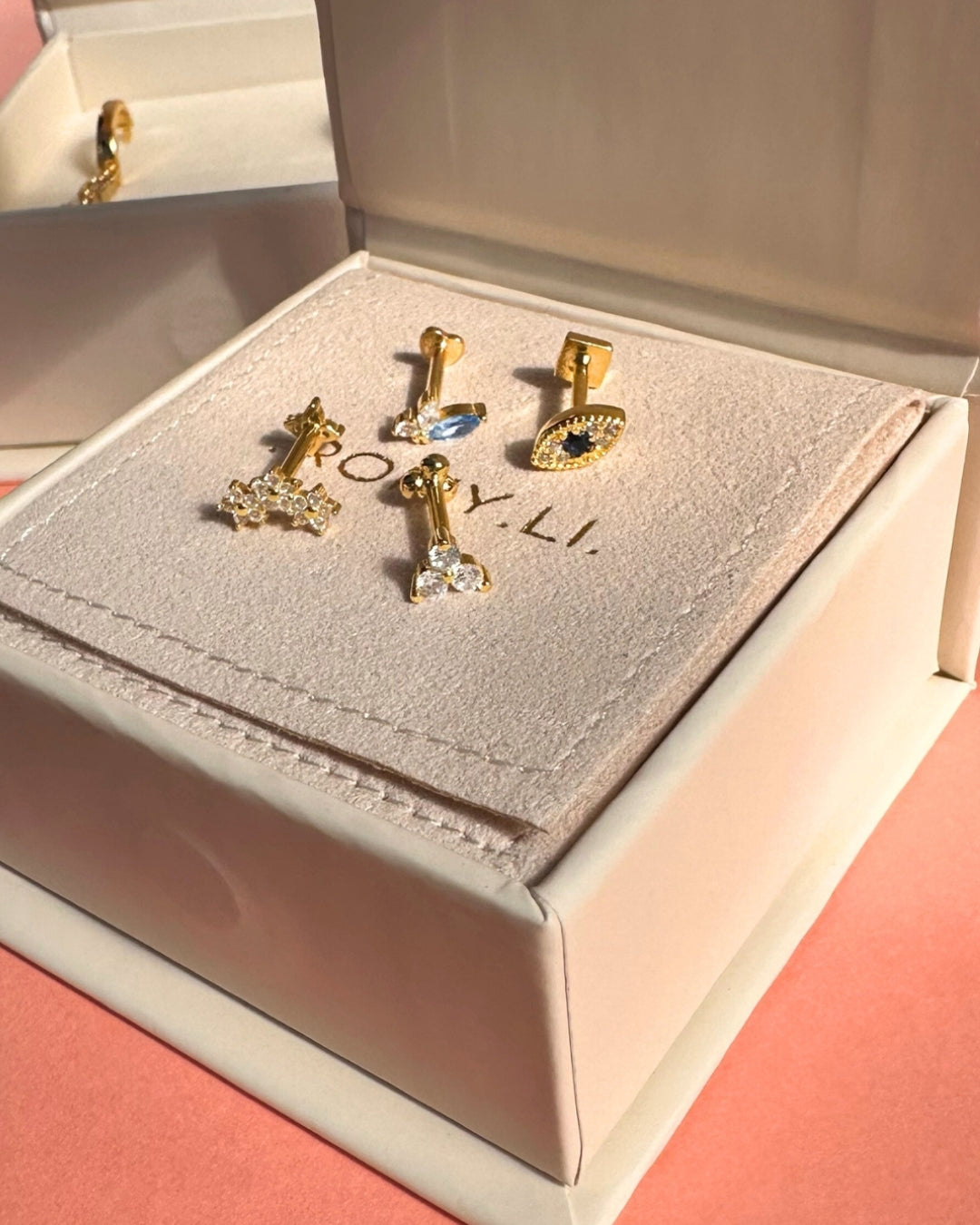 Reversible gold vermeil flatback stud earring featuring a front evil eye design with white and sapphire-blue crystals and a polished gold square backing, displayed in a Romyli gift box.