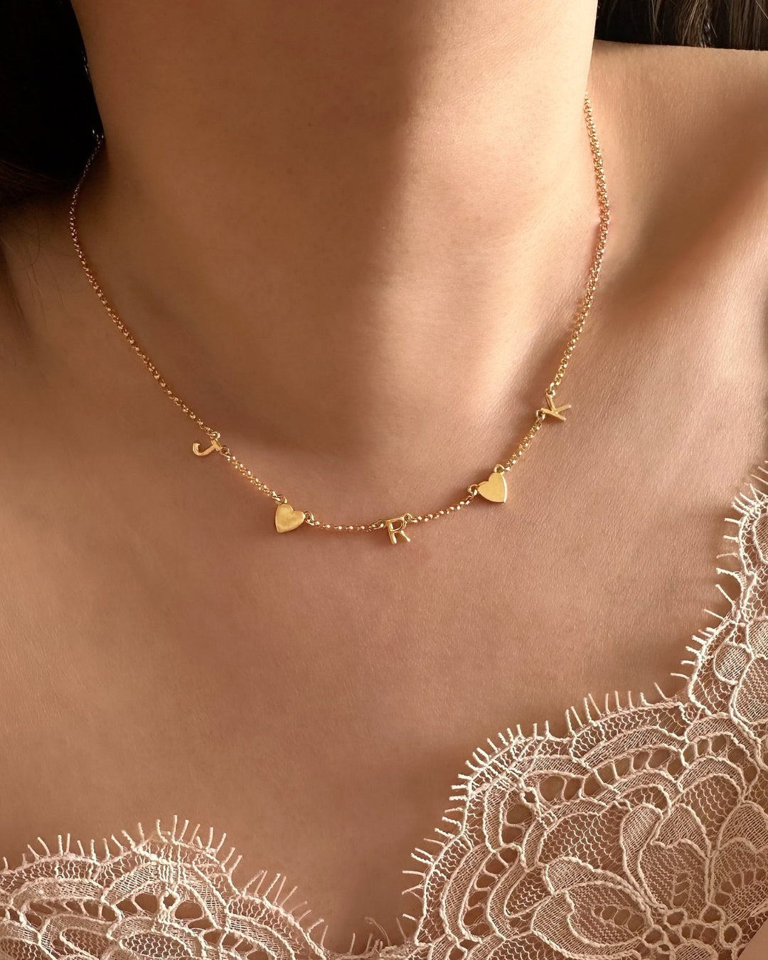 Model wearing Gold-filled necklace with 3 letter charms and 2 gold heart charms evenly spaced on a petite rolo chain. 