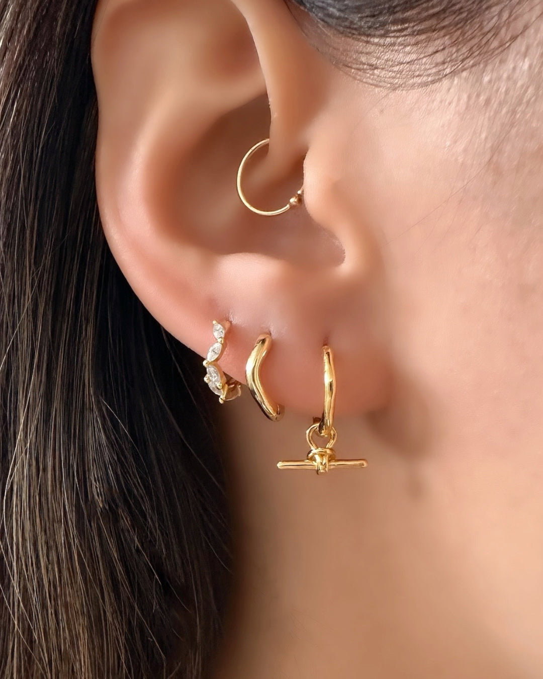 Model wearing Gold huggie earrings with marquise cut huggies, gold organic wave huggies and T-bar charm Huggies. 