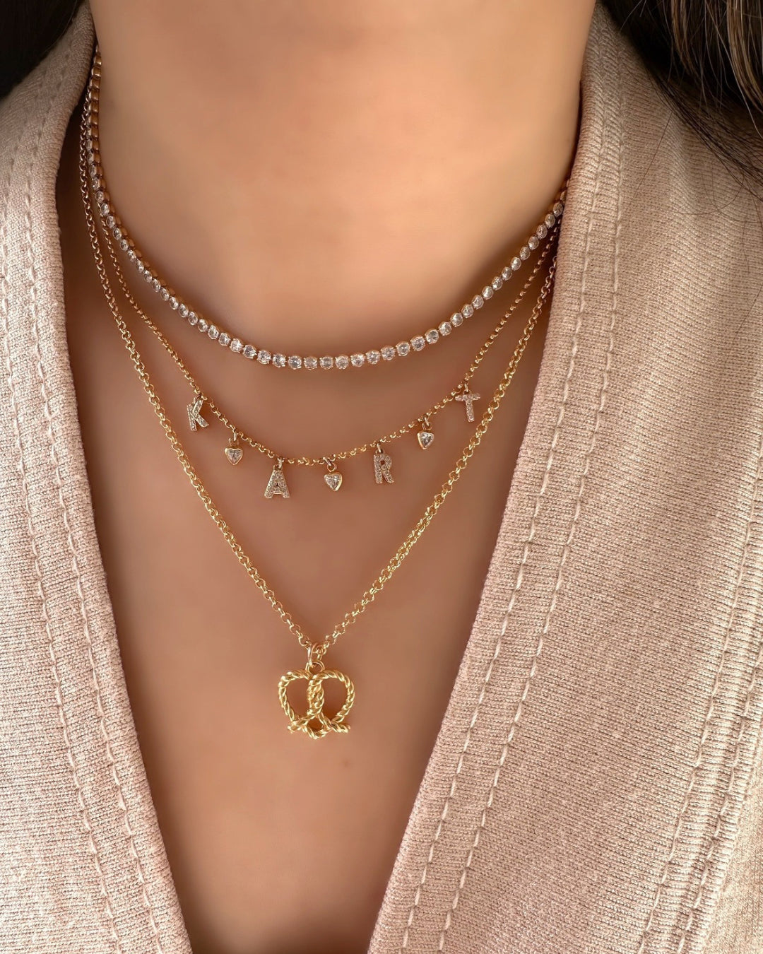 Model wearing 2mm gold tennis choker necklace with bezel cubic zirconia crystals, layered with gold Pavé Initial Necklace and Gold Pretzel Heart Necklace 