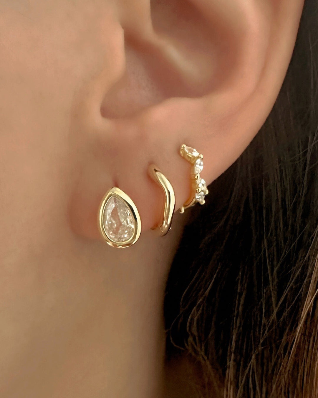 Gold earrings worn on an ear, Gold Vermeil Teardrop Bezel Huggie, Curvature Huggies (second lobe) and  Fleck Marquise Huggies (third lobe). 