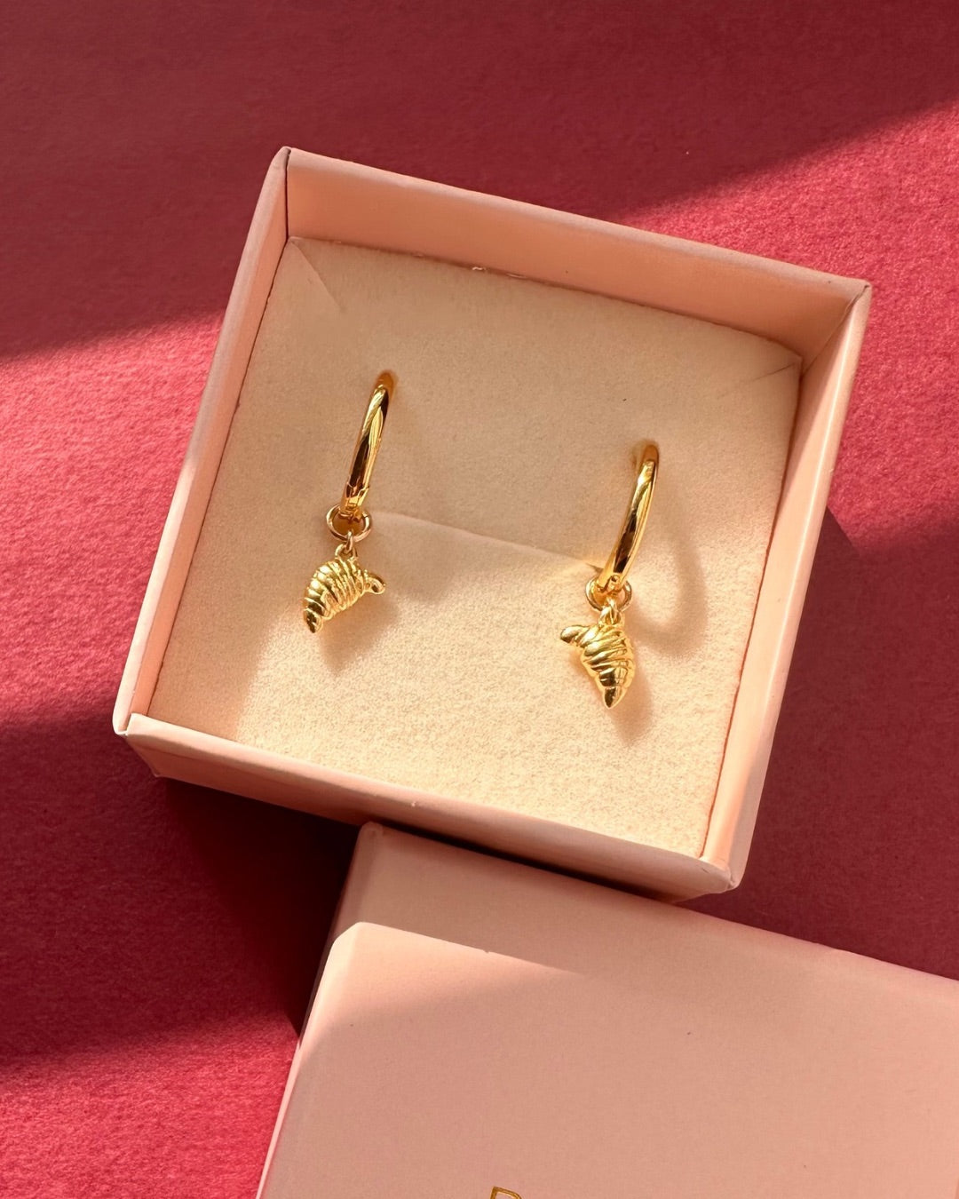 Gold croissant charm hoops in a pink Romyli gift box on a maroon background 