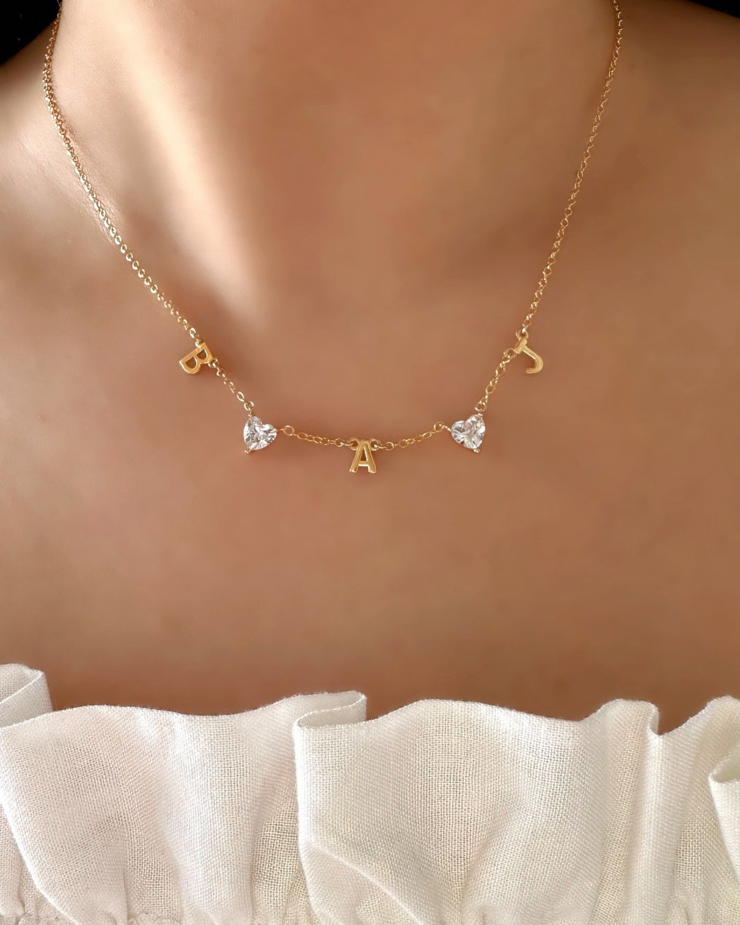 Model wearing custom gold-filled necklace with 3 initial letter charms and 2 heart gems evenly spaced on a petite rolo chain. 
