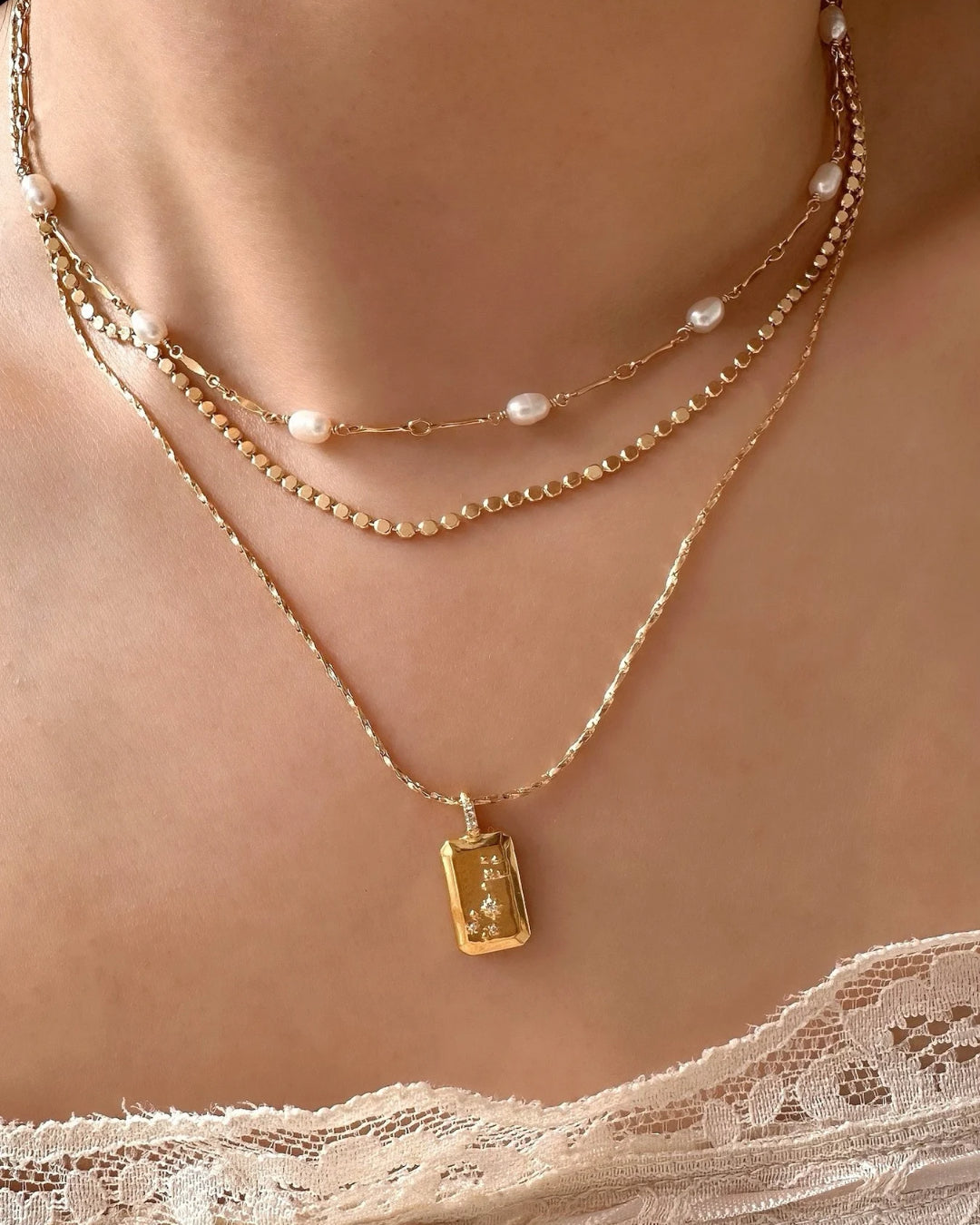 Model wearing layered gold necklaces featuring a Scorpio constellation pendant, dainty petite faceted necklace, and Opalene pearl choker with freshwater pearls.