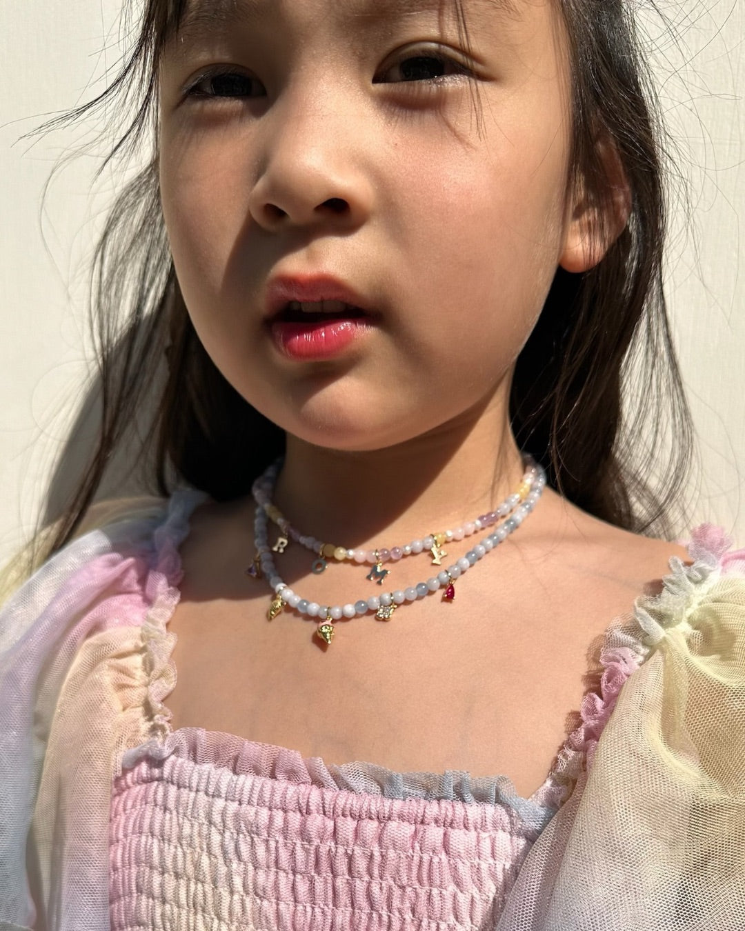 Young girl wearing a colorful pastel gemstone charm necklace against a neutral background
