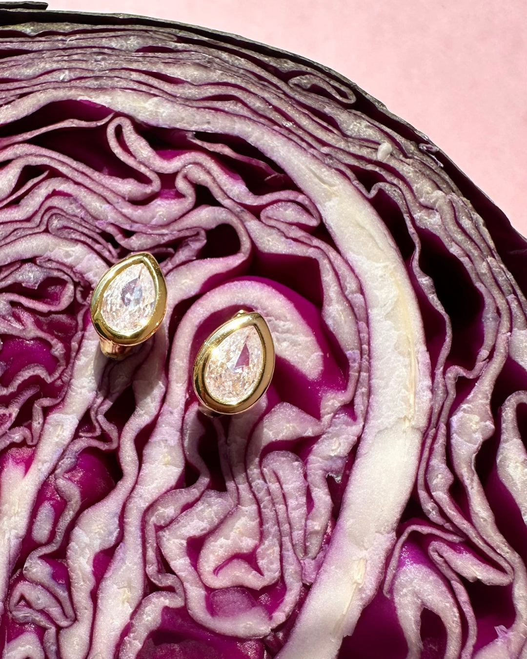 Gold teardrop bezel Huggie hoop earrings with clear stones on a sliced red cabbage background