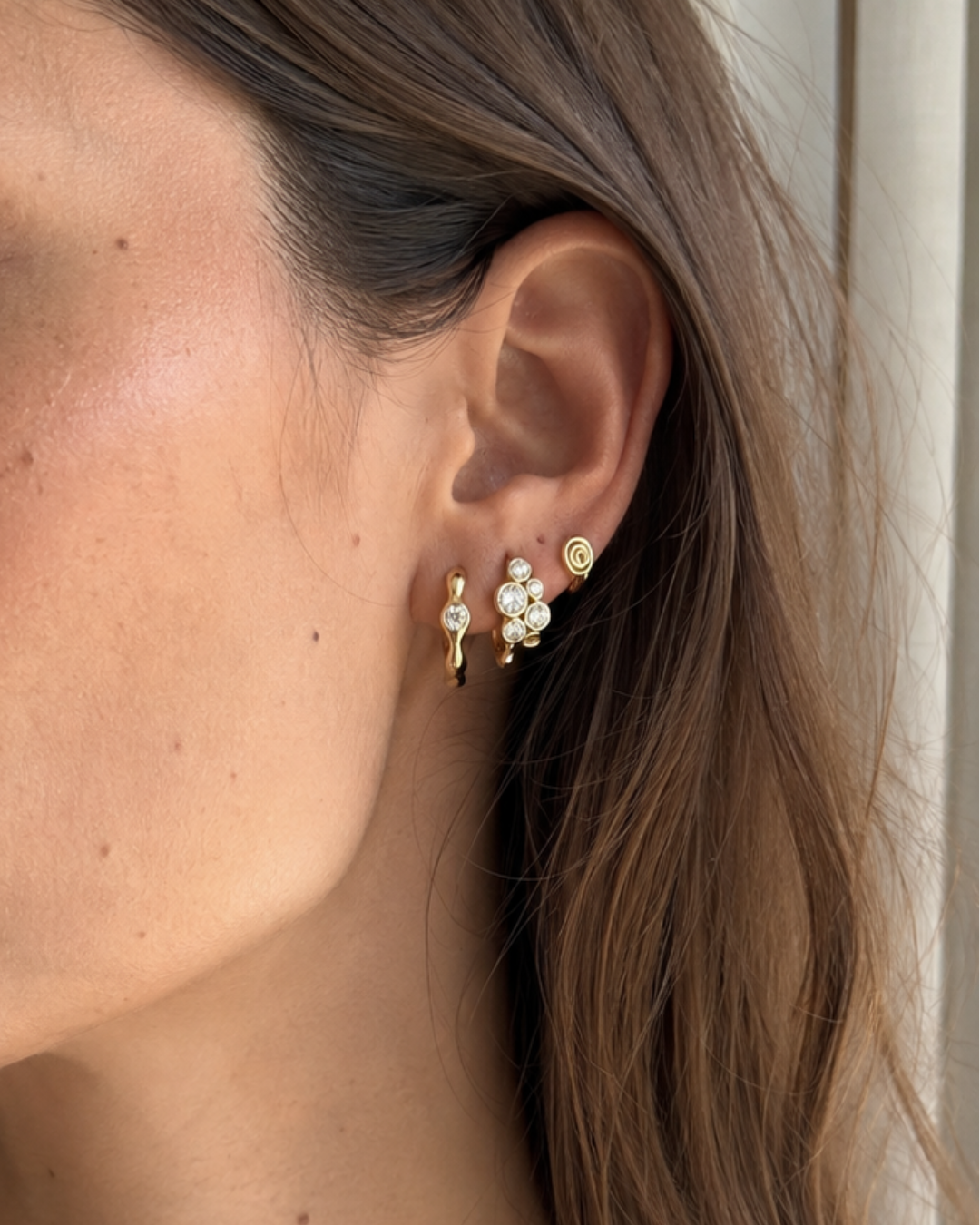 Woman wearing sculpted hoops, bubble cluster Huggies and spiral huggies 