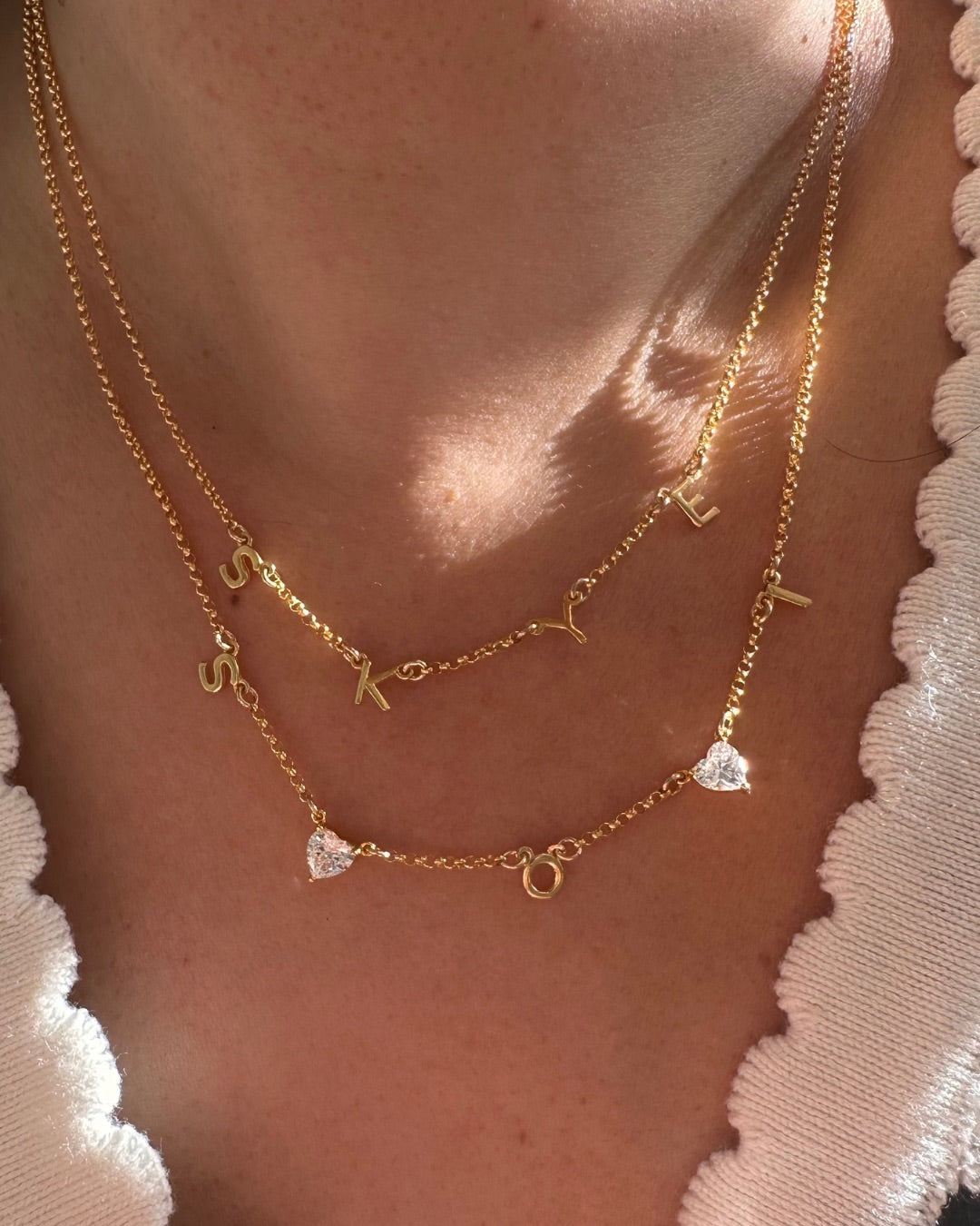 Gold necklaces with letter pendants on a person's neck