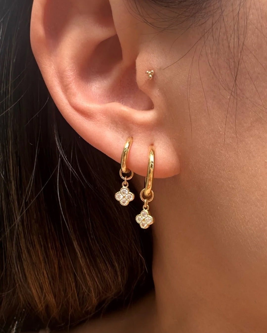 Model wearing Gold Mini Clover Charm Hoops. First ear lobe features the Medium hoops and second earlobe features the Small hoops.