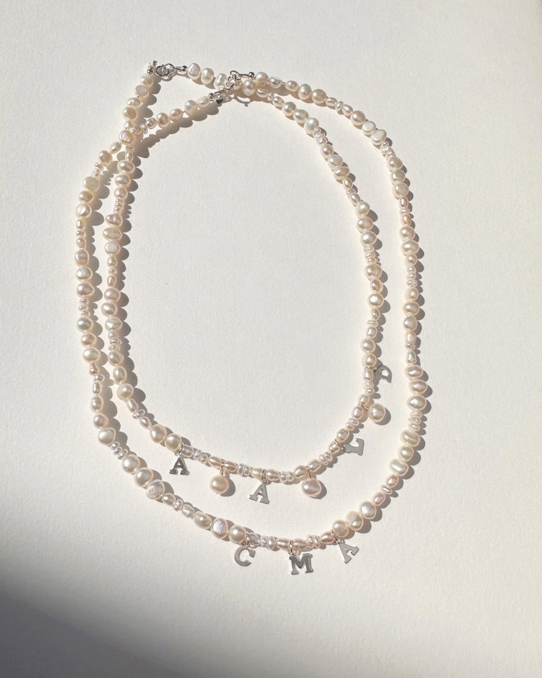 Two pearl necklaces with letter and mini pearl charms on a white background