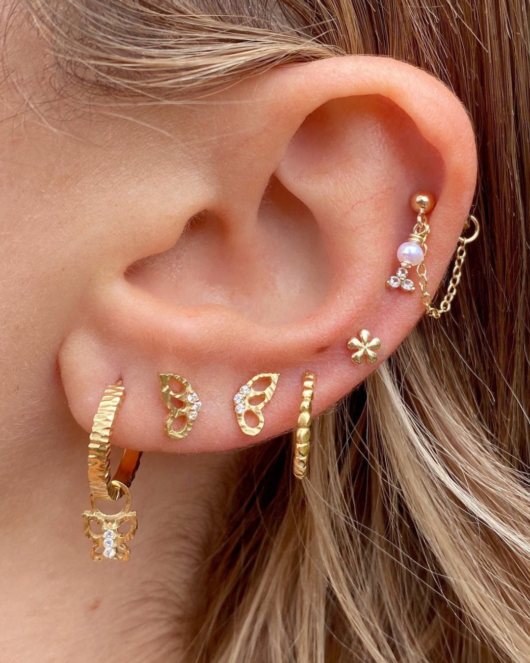 Gold butterfly flutter stud earrings stacked with gold hoop earrings and solid gold Flatback studs on a model 