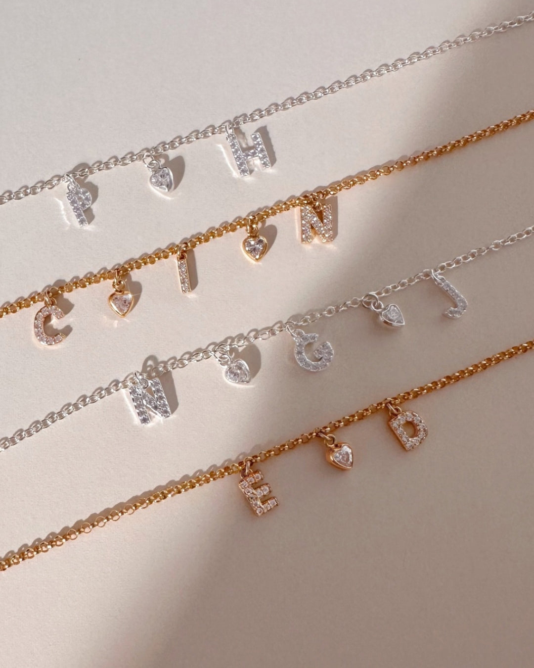 Flatlay of gold and silver pavé initial bracelets with dainty custom letters and heart charms, personalised jewellery in gold fill and sterling silver