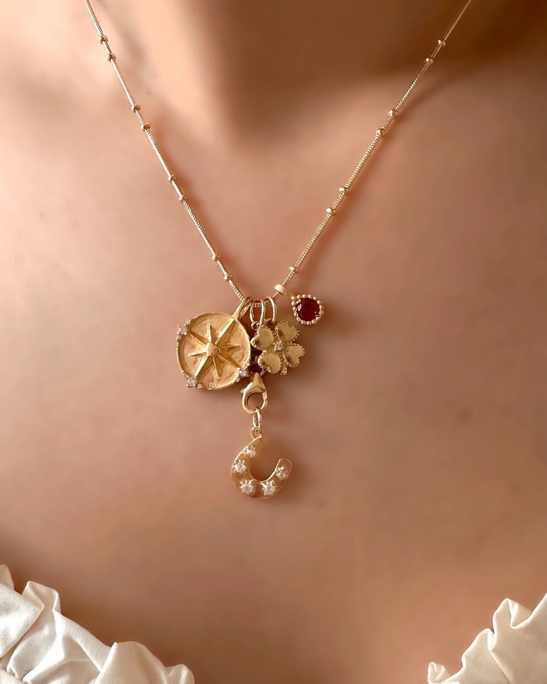 Model wearing Romyli Mix & Match Pendants with Gold Beaded Necklace. Horseshoe Talisman Pendant with Rolo Pendant Chain Connector, Dreamers Pendant and Clover Talisman and July Birthstone (Ruby) Pendant 