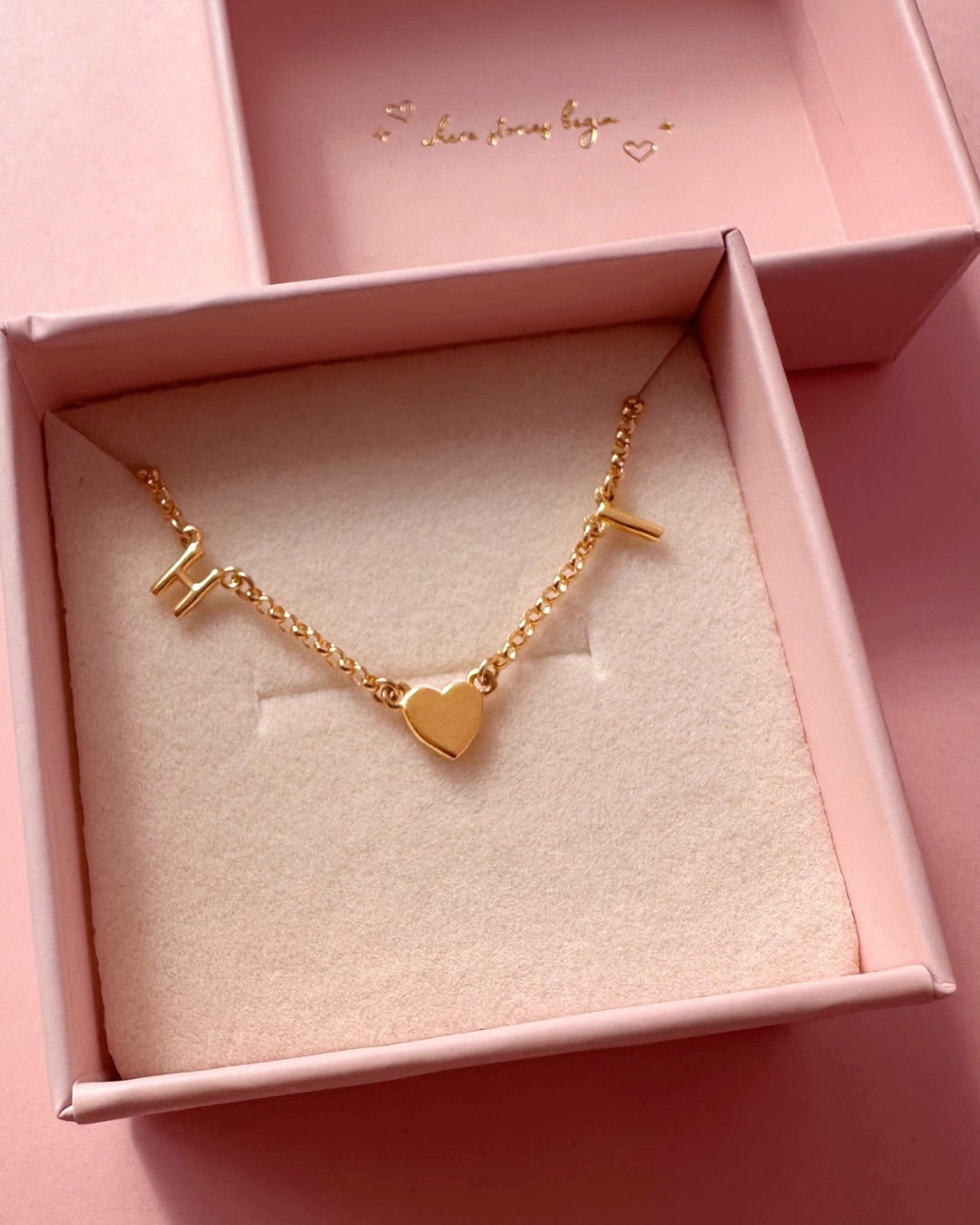 Gold initial bracelet with gold letters and gold heart charm in a pink Romyli gift box. 