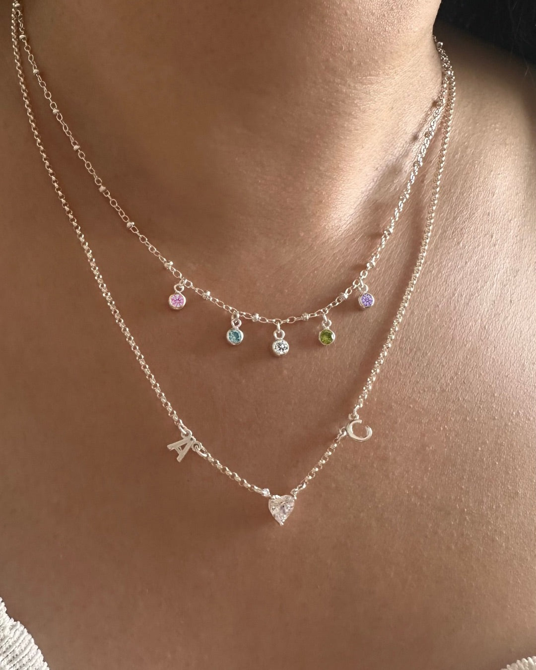 Necklace with silver petite Initial necklace and petite birthstone necklace on a model’s neck