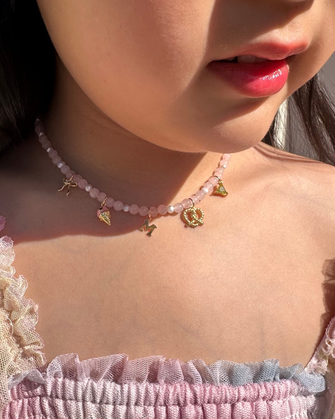 Close-up of a person wearing a rose quartz charm necklace with small gold filled charms.