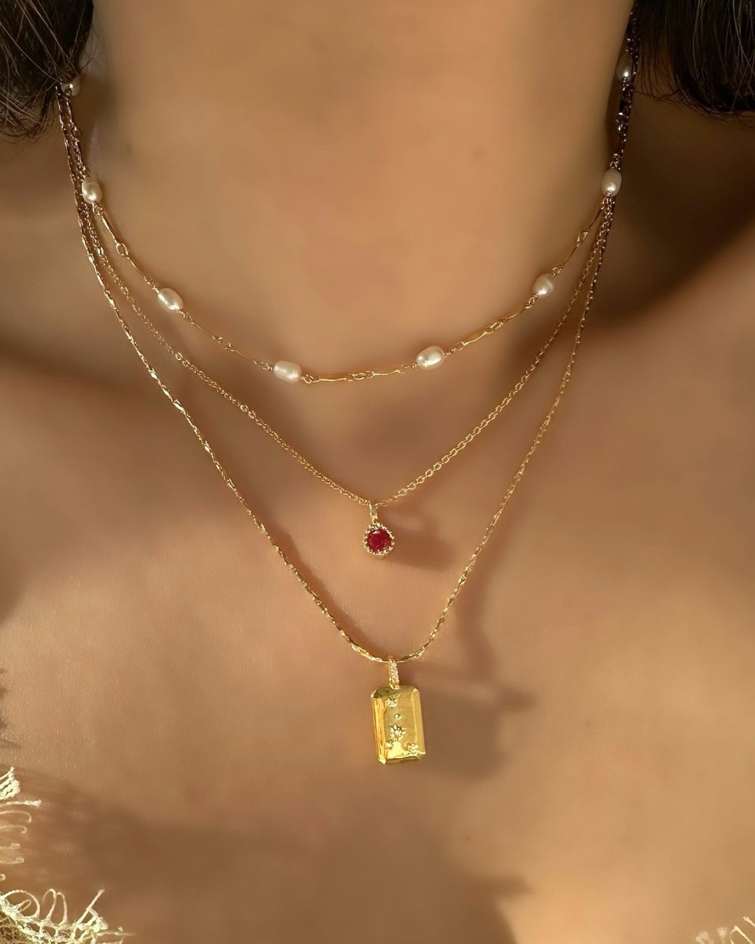 Gold Cancer Constellation Zodiac Pendant on a Gold Necklace Chain layered with Ruby Birthdstone Necklace and Opalene Pearl Choker on a model 