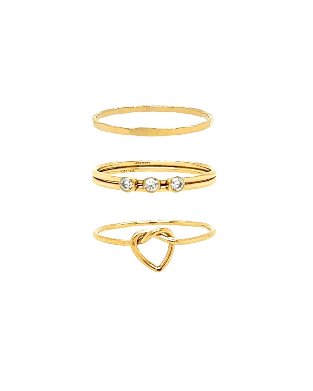 A close-up of the Classic Trio Ring Set, featuring a delicate trio ring with three cubic zirconia stones on a double band, a love knot ring, and a faceted ring, all stacked together for a refined and modern look.