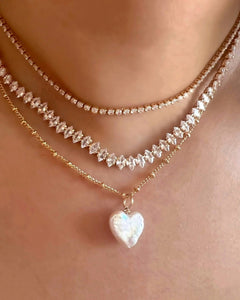 Gold Pearl heart necklace layered with petite tennis necklace and marquise tennis necklace on a model