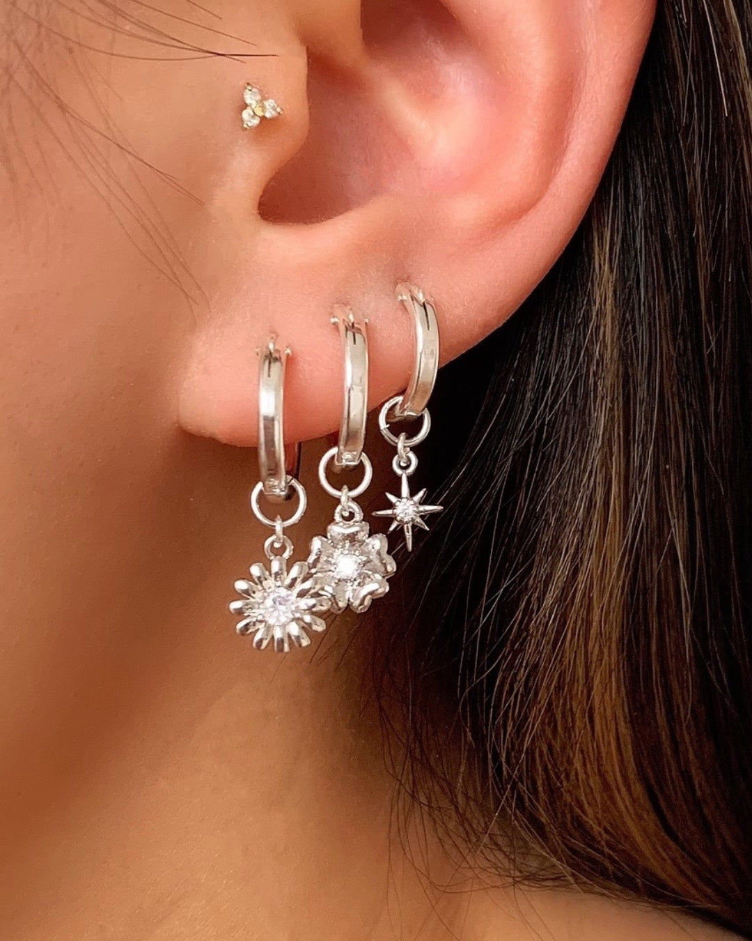 Sterling Silver Small Hoop Earrings with Silver Daisy, Fleur and North Star Earring Charms on a model. 
