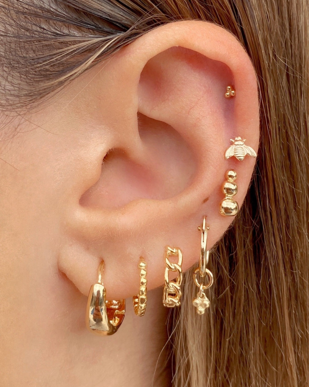 Gold trio stud earrings stacked with gold hoops Huggies and gold Flatback stud earrings on a model 