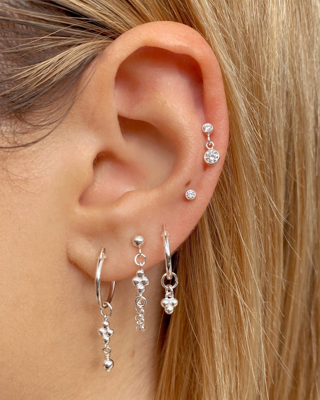 Sterling silver bezel stud earrings layered with silver hoops and silver drop stud earrings on a model 