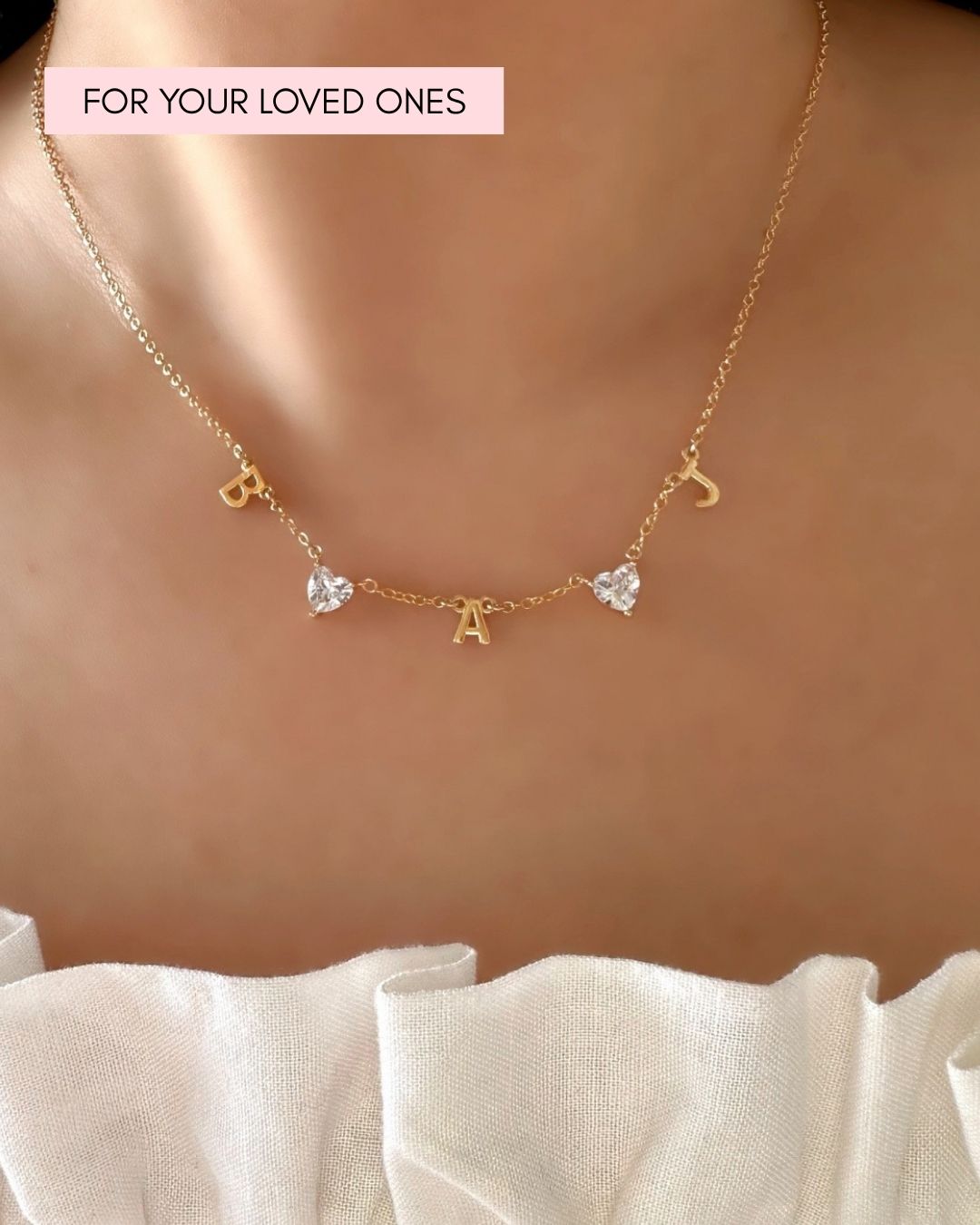 Model wearing custom gold-filled necklace with 3 initial letter charms and 2 heart gems evenly spaced on a petite rolo chain. 