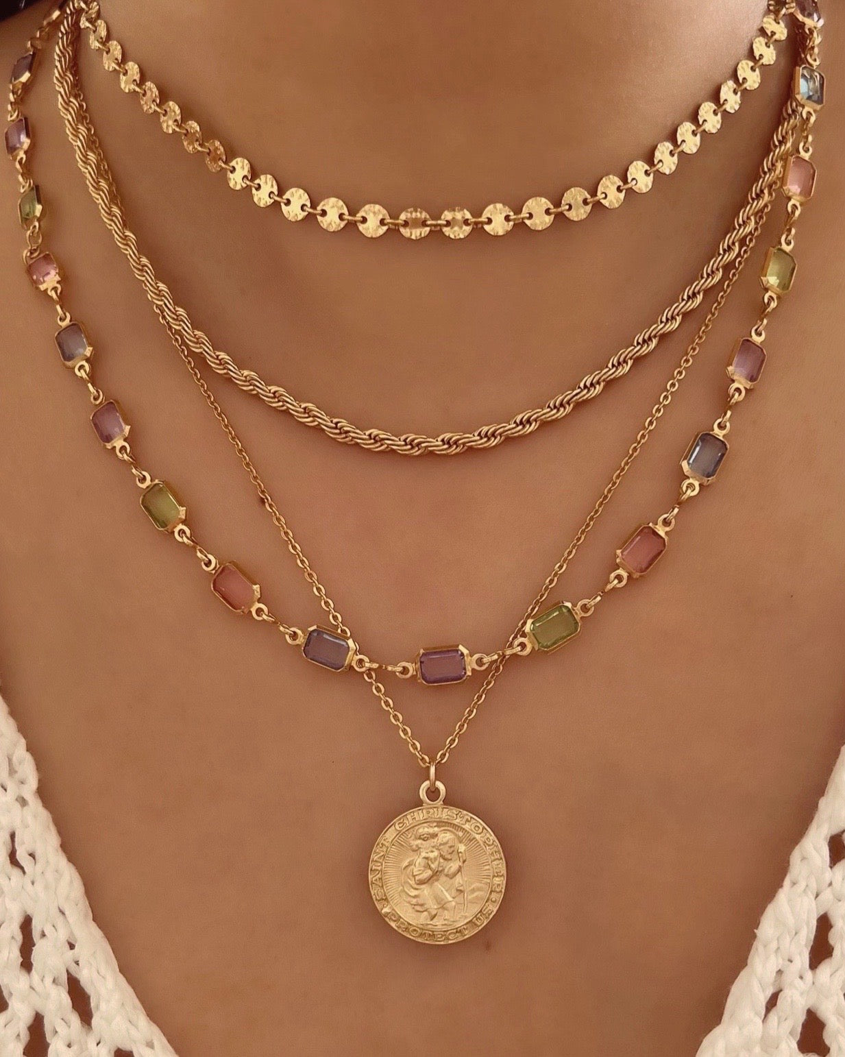 Gold fill necklace in pink, blue and purple bezel gems on a model layered with gold necklaces and St Christopher necklace 